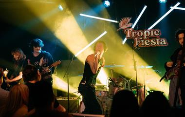 Four artists on stage with microphones and musical instruments.