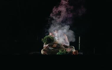 A man sitting on stage while performing a cultural piece.